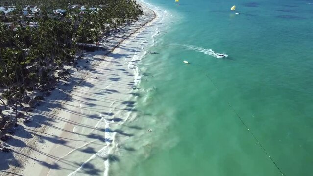 Wakacyjna plaża z palmami na karaibach, a obok turkusowy ocean z delikatnymi falami. Jest to nadmorski kurort turystyczny.