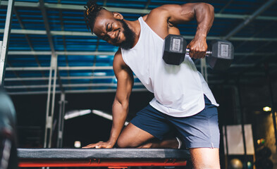 Black man doing exercise with dumbbell over bench