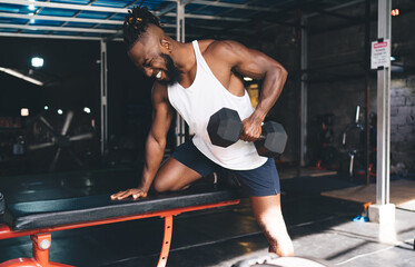 Strong ethnic sportsman doing exercises with dumbbell - obrazy, fototapety, plakaty