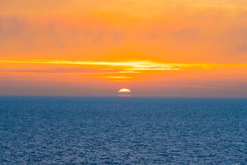 Naklejka na ściany i meble Beautiful Sunset in the Atlantic Ocean with orange sky and blue ocean somewhere in Faroe Islands