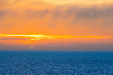 Naklejka na ściany i meble Beautiful Sunset in the Atlantic Ocean with orange sky and blue ocean somewhere in Faroe Islands