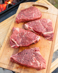 Four beef steaks lie on a cutting board next to the grill