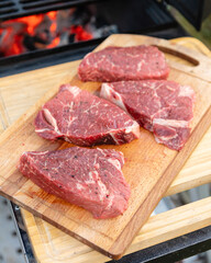 Four beef steaks lie on a cutting board next to the grill