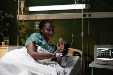 Woman in hospital bed waving, African, holding phone and smiling.