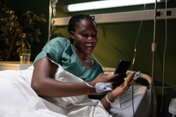 Hospital scene with the African woman, lying down and grinning at her phone, captivated by an...
