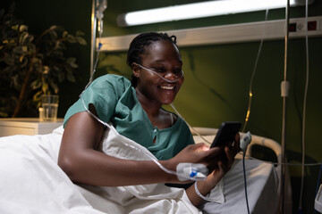 Photo of the African woman in the hospital, propped on her elbow, chuckling at a funny video on her...