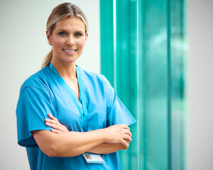 Portrait Of Mature Smiling Female Doctor Wearing Scrubs In Hospital - obrazy, fototapety, plakaty