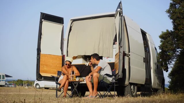 Couple with a dog eating Nachos and drinking beer for dinner outside their camper van