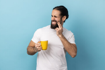 Portrait of man with beard wearing white T-shirt standing and touching his cheek because feeling...
