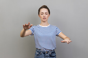 I'm blind. Portrait of woman wearing striped T-shirt walking with closed eyes, stretching hands to...