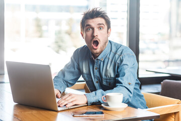 Portrait of amazed astonished surprised man freelancer in blue jeans shirt working on laptop,...