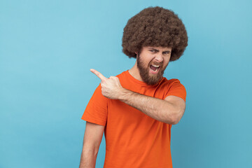 Portrait of man with Afro hairstyle wearing orange T-shirt pointing to the side and turning away...