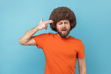 Portrait of frustrated anxious man with Afro hairstyle keeps eyes closed, holding fingers gun...