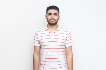 Portrait of strict serious bossy bearded man wearing striped t-shirt standing looking at camera,...