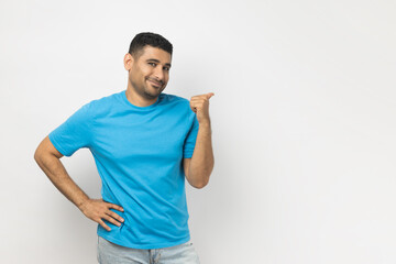 Portrait of smiling satisfied young adult unshaven man wearing blue T- shirt standing indicating at...