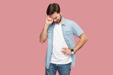 Portrait of depressed crying bearded man standing being in stressful situation stands desperate as faces problem feels regret blames himself in failure. Indoor studio shot isolated on pink background.