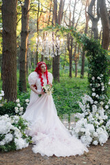 Obraz na płótnie Canvas Beautiful couple, the groom in a green suit and the bride in an unusual pink wedding dress, posing at a luxurious ceremony with beautiful decor and an arch with a chandelier and candles in the forest 