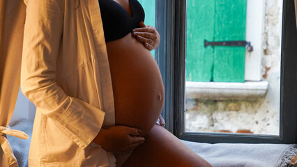  pregnant woman with hands on belly sitting near window at home.  