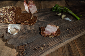 Making a sandwich with bacon and black bread. Garlic and spices. Hard light. Old wooden table.