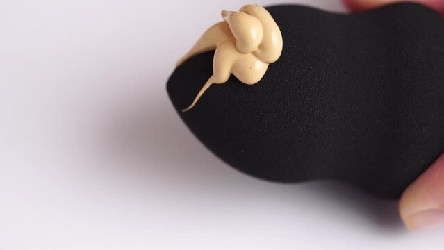 Make-up liquid beige foundation pouring on black sponge, closeup. BB Cream dripping on beauty blender on white background. Macro Shot. Beautiful Makeup concept.