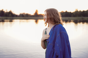 Portrait of happy cute smiling attractive traveler teenager girl wearing green dress blue shirt standing alone on pier with lake on blurred background.
