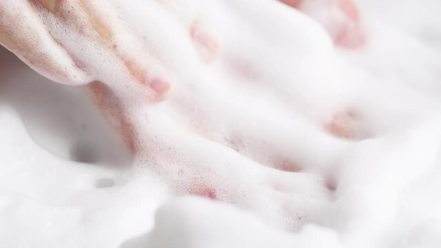 Female hands are washing with soap bubbles. Woman plays with fluffy foam in bathtub, macro. Lady holds handful of soap bubbles, close up.