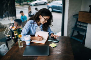 Focused woman taking notes from smartphone in cafe