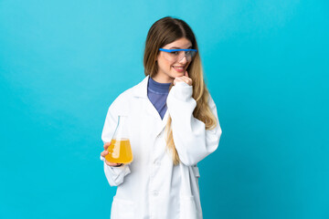 Young blonde scientific woman isolated on blue background looking to the side and smiling