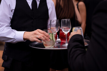 Bandeja con bebidas siendo servidas por mozo, no rostros, sólo manos 