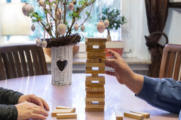 At Easter, the family plays board games together. Wife and husband build a wobbly tower out of wooden blocks. In the background is the Easter bouquet with Easter eggs. Motion blur.