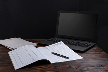 Financial notebook on the table and laptop nearby. Notebook and pen on the table. Maintaining records and finances. Planning and tasks.