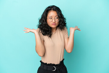 Young asian woman isolated on blue background having doubts while raising hands
