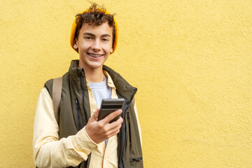 Smiling millennial boy, teenager with dental braces holding mobile phone looking at camera isolated...