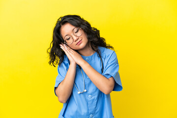 Young surgeon doctor asian woman isolated on yellow background making sleep gesture in dorable...