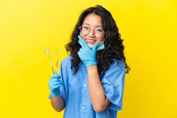 Young asian dentist holding tools over isolated background happy and smiling