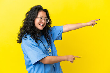 Young surgeon doctor asian woman isolated on yellow background pointing finger to the side and...