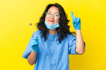 Young asian dentist holding tools over isolated background pointing up a great idea