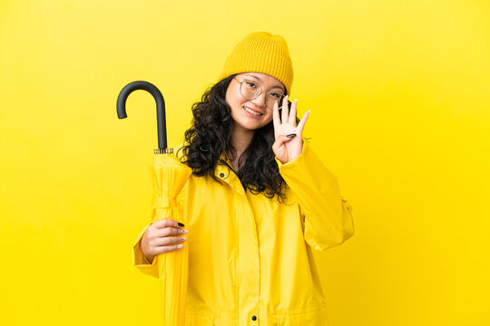 Asian woman with rainproof coat and umbrella isolated on yellow background happy and counting four with fingers