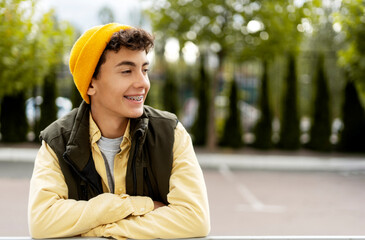 Smiling confident millennial boy,  teenager wearing yellow hat with dental braces looking away,...