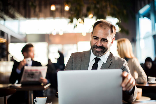 Happy businessman sitting in cafe using laptop