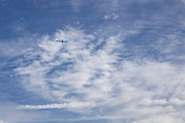 Fototapeta na wymiar Blue plane in the clear blue sky with some cloud cover