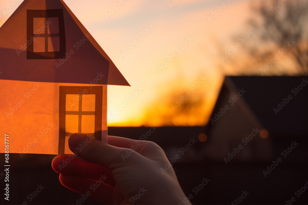 Wall mural Hands holding a paper-cut house shape against a sunset background