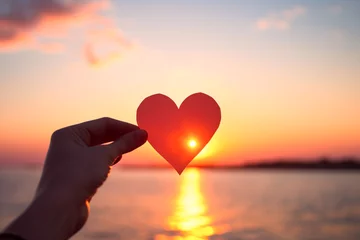 Tuinposter Hands holding a paper-cut heart shape against a sunset background © artsterdam