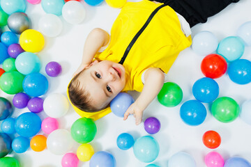 Fototapeta na wymiar Happy boy in colorful balls in children's playgroup. the child smiles, hiding in the balls.