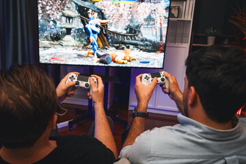 Friend gamers playing video game of battle martial arts fighter on TV using joysticks position of...