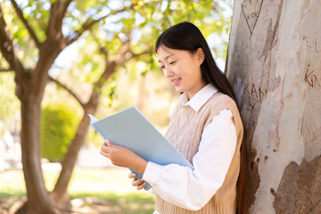 Pretty Chinese woman at outdoors holding a notebook