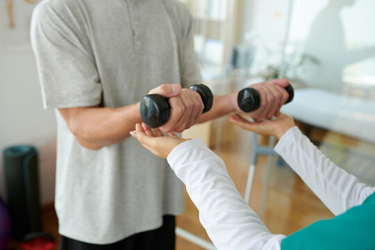 Physiotherapist helping patient to do fitness exercises with light weight dumbbells