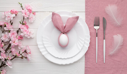 Festive Easter table setting with bunny made of pink linen napkin and egg. Top view. Happy Easter holiday concept for restaurant menu. Empty plate and cutlery on white wooden background. Flat lay.