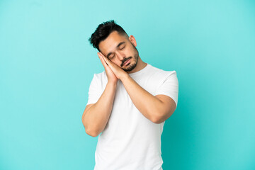 Young caucasian man isolated on blue background making sleep gesture in dorable expression