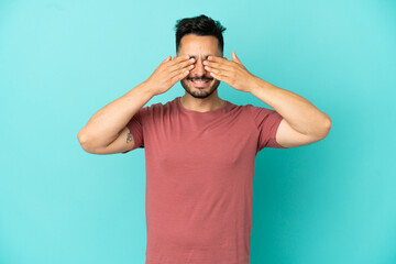 Young caucasian man isolated on blue background covering eyes by hands and smiling